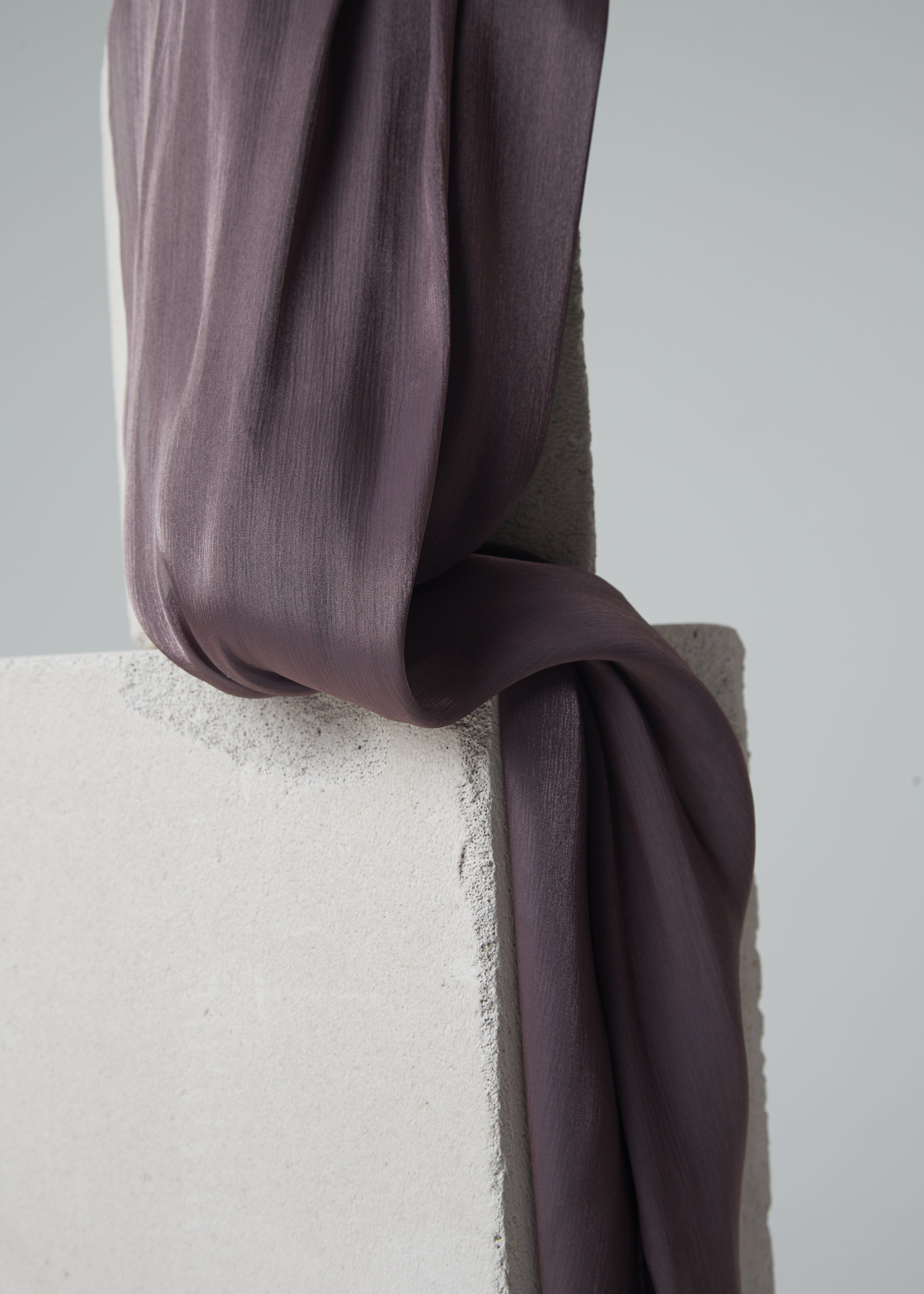 Mauve silk hijab draped over textured concrete blocks — soft matte finish with a subtle pearlescent sheen, styled for minimalist product display.