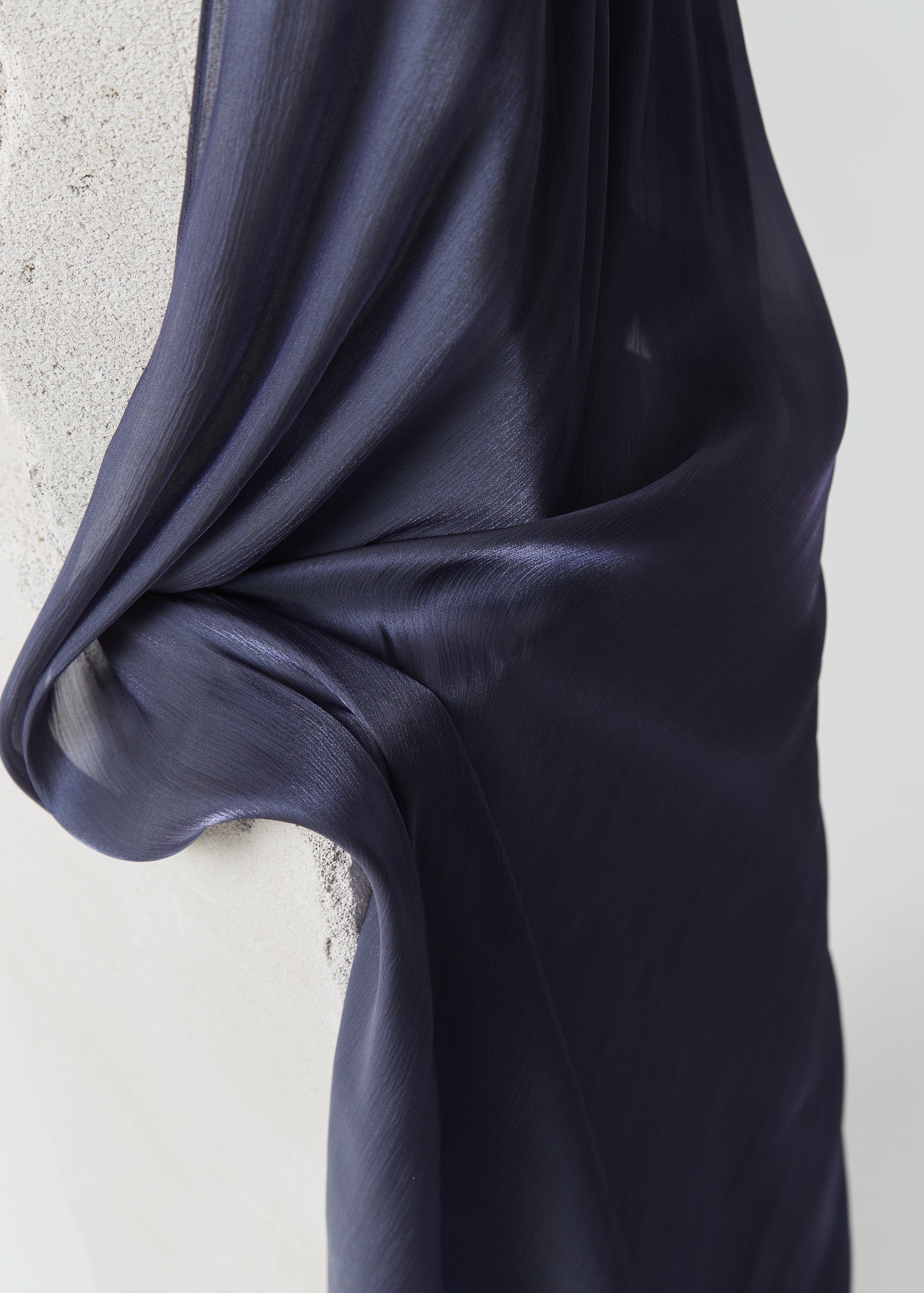 Deep midnight blue silk scarf from Yovlaq draped over a textured concrete block – premium lightweight fabric with elegant sheen.