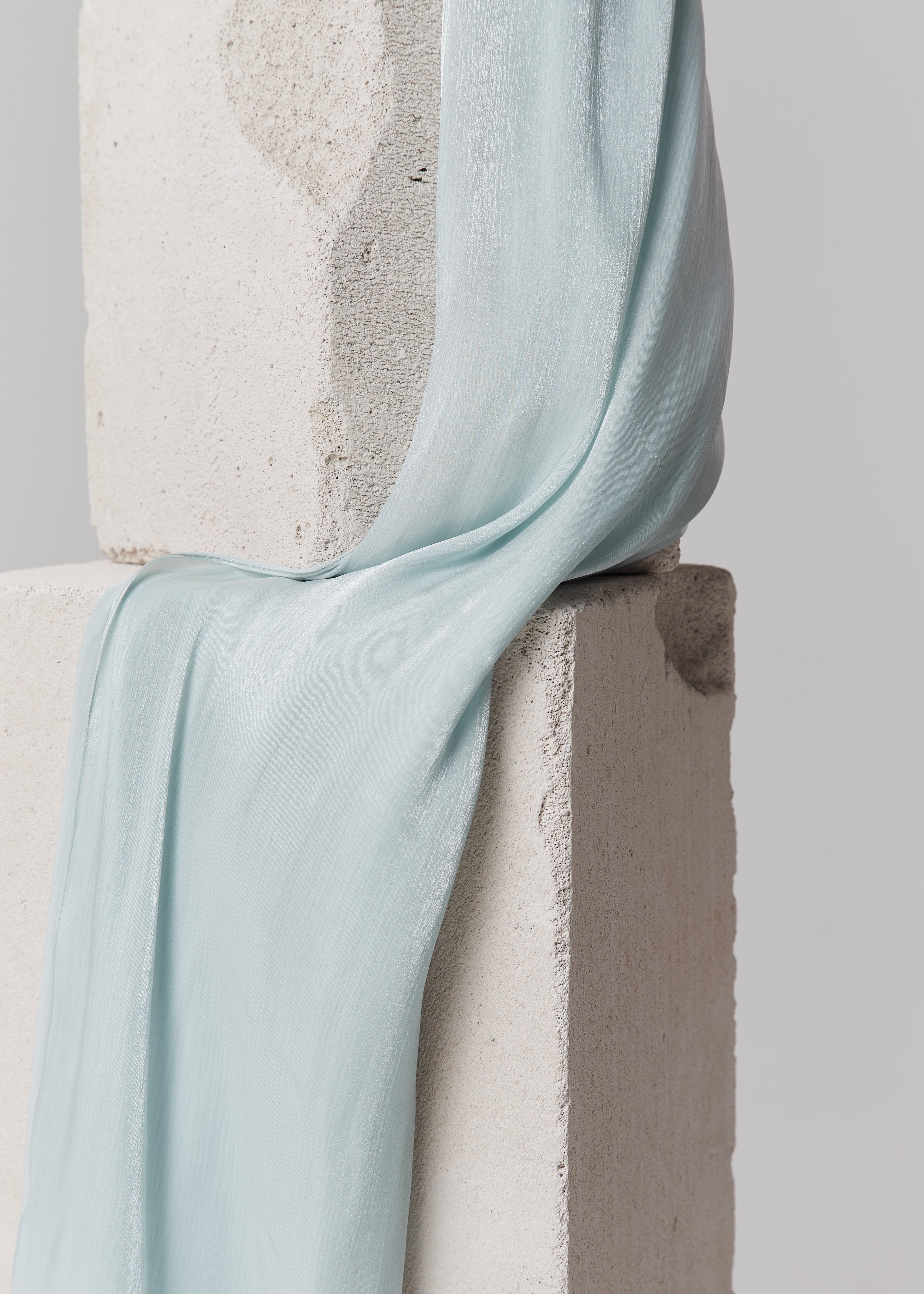 Mint cream silk chiffon scarf from Yovlaq draped over textured concrete blocks – luxury handmade accessory for women