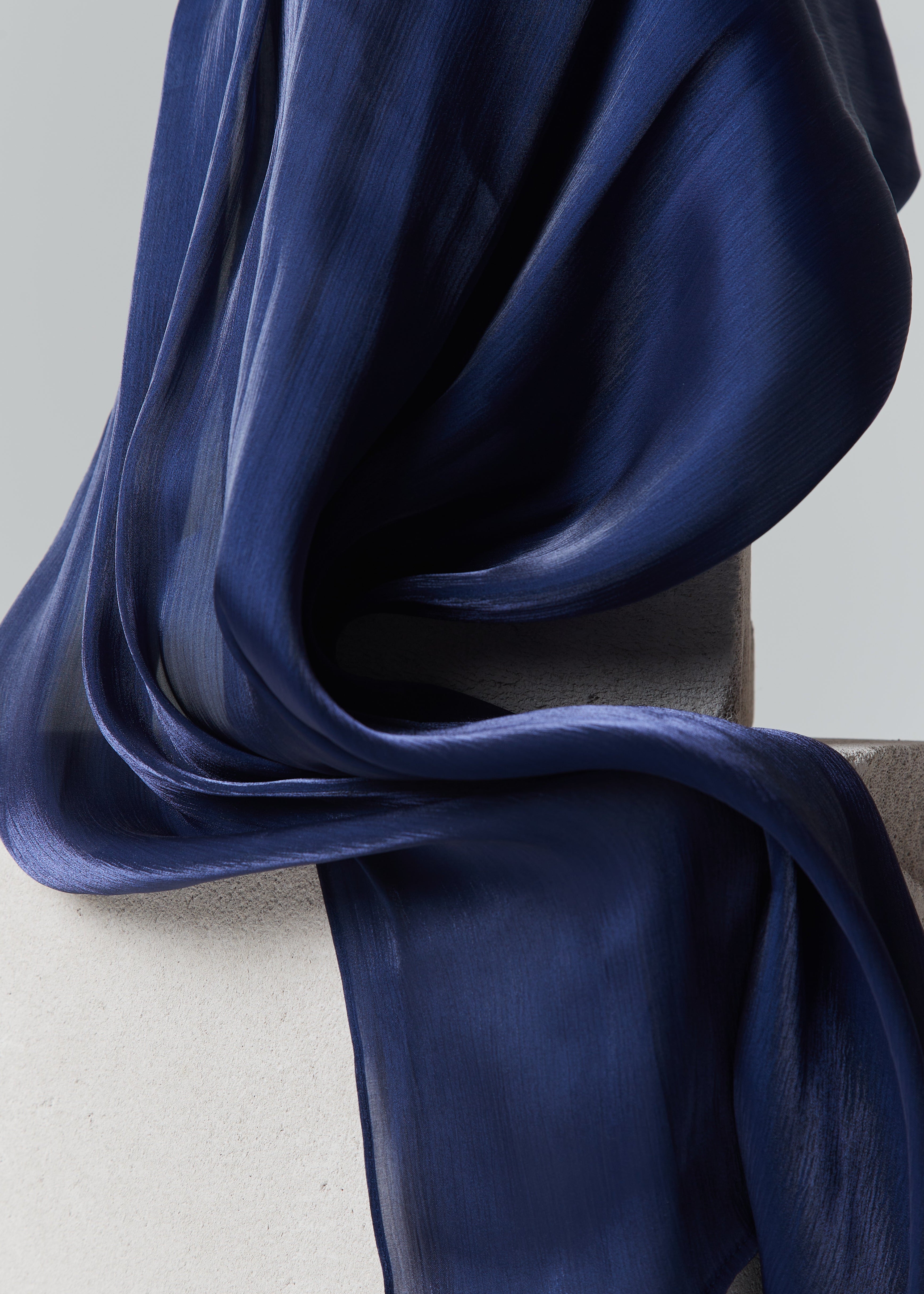 Elegant navy blue ready-to-wear silk hijab draped over matte stone blocks, highlighting its rich colour and fluid texture.
