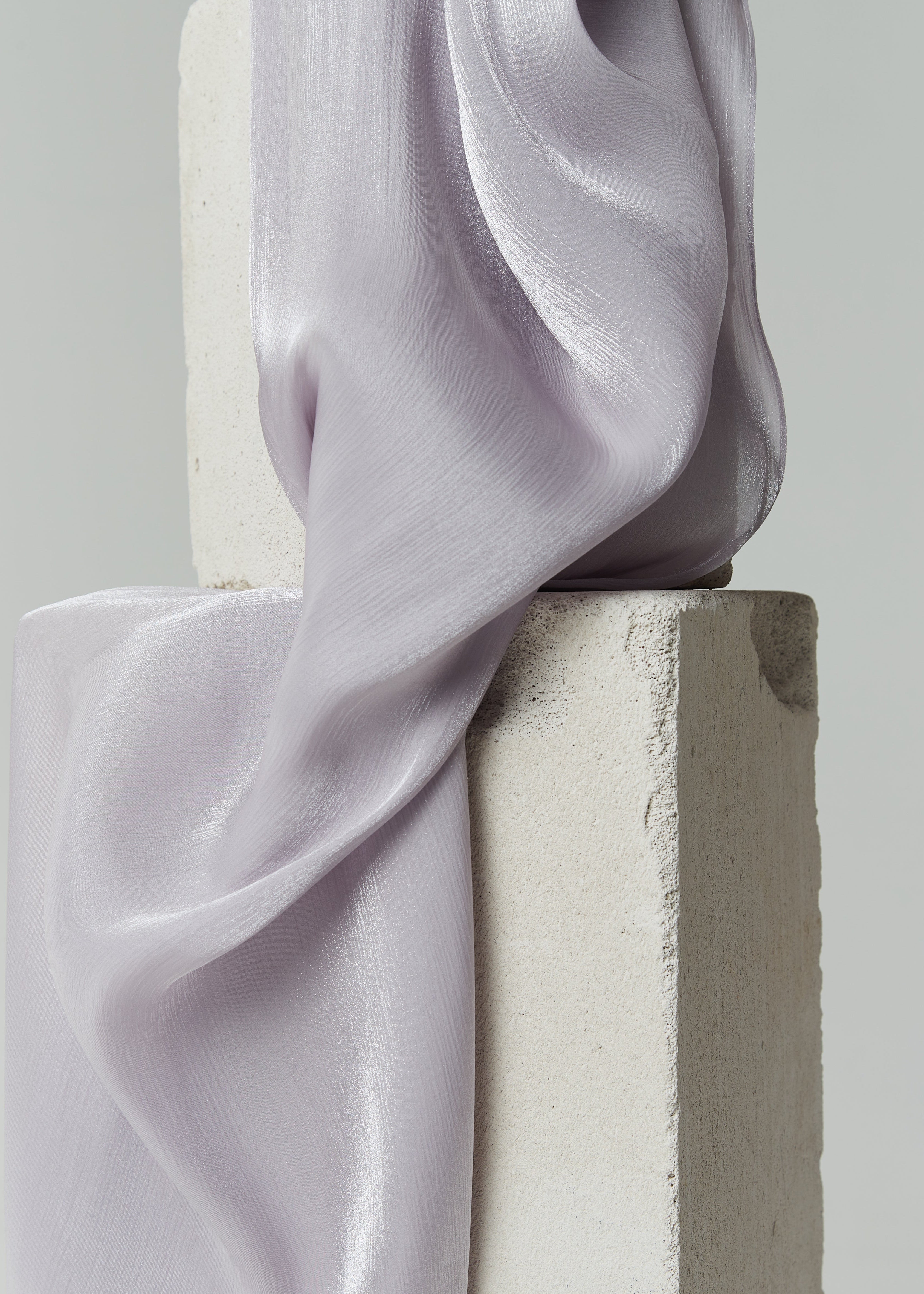 Close-up of pale purple lavender silk hijab by Yovlaq draped over concrete blocks – soft, flowing texture with elegant semi-sheer finish.