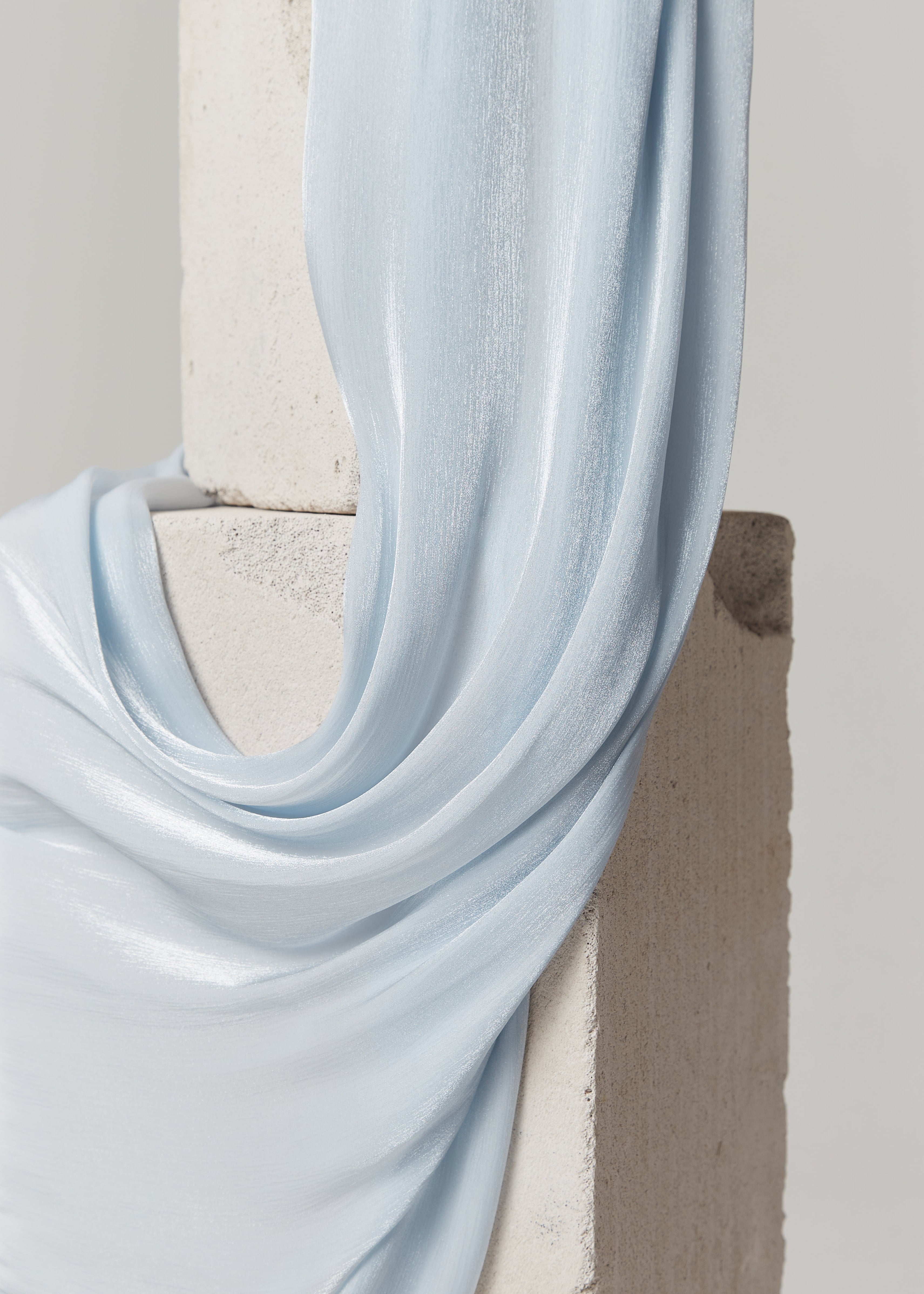 Close-up of pastel blue silk hijab from Yovlaq draped over stone blocks – lightweight, glossy finish with elegant texture.