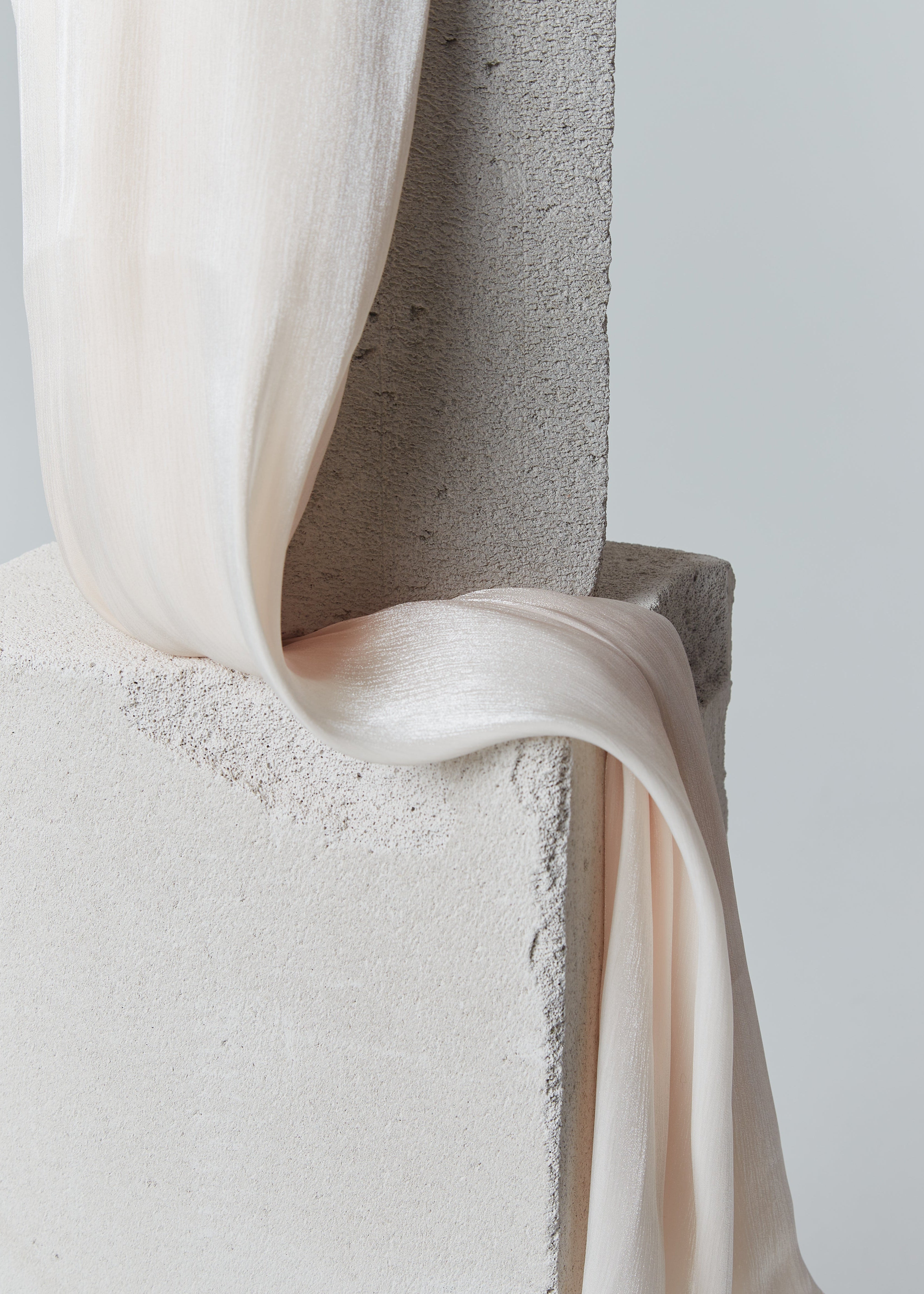 Soft peach ready-to-wear silk hijab draped over textured stone blocks, showcasing its smooth, semi-sheer finish and graceful flow.