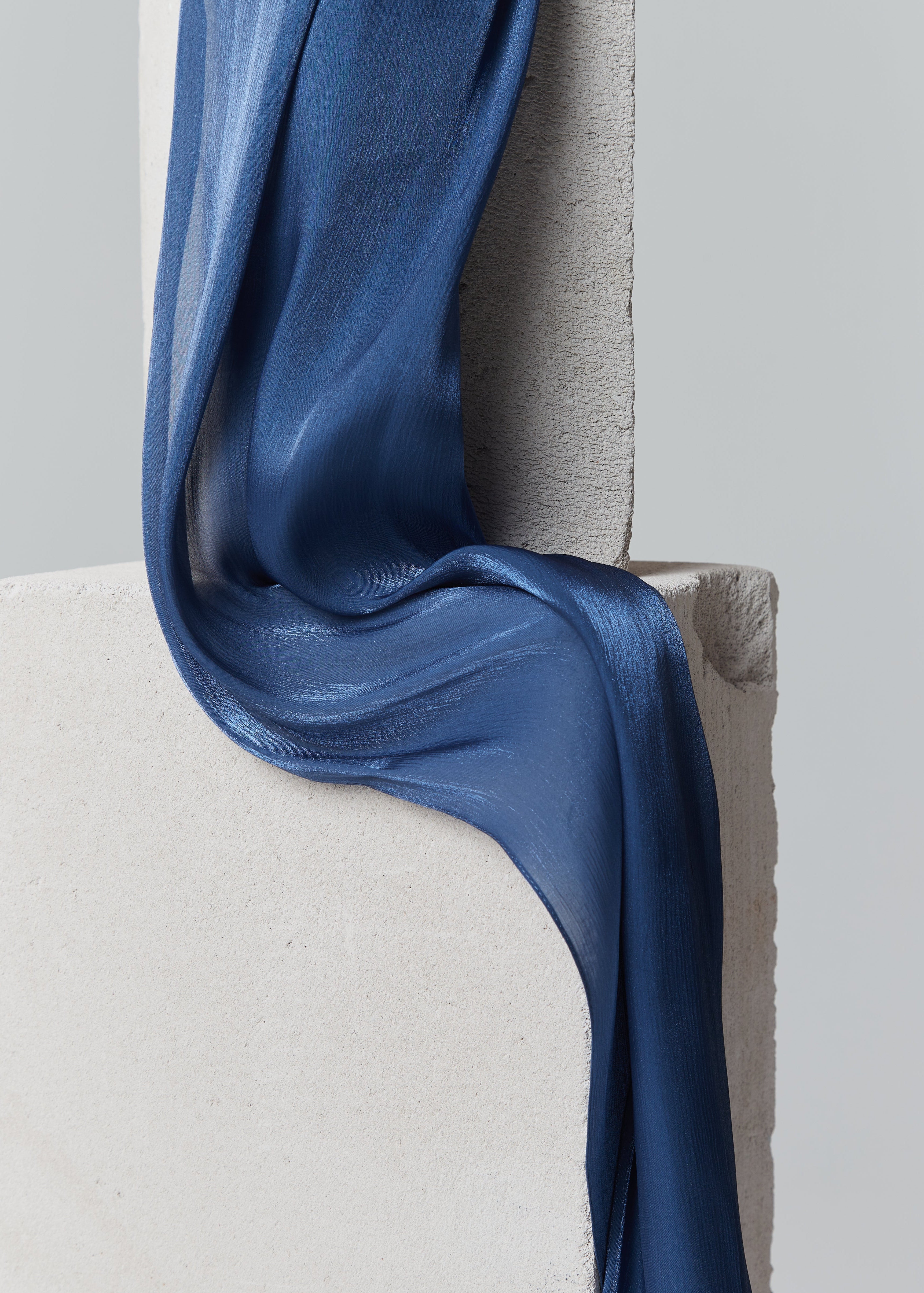 Steel blue ready-to-wear silk hijab elegantly draped over minimalist cement blocks, showcasing its smooth texture and subtle sheen.