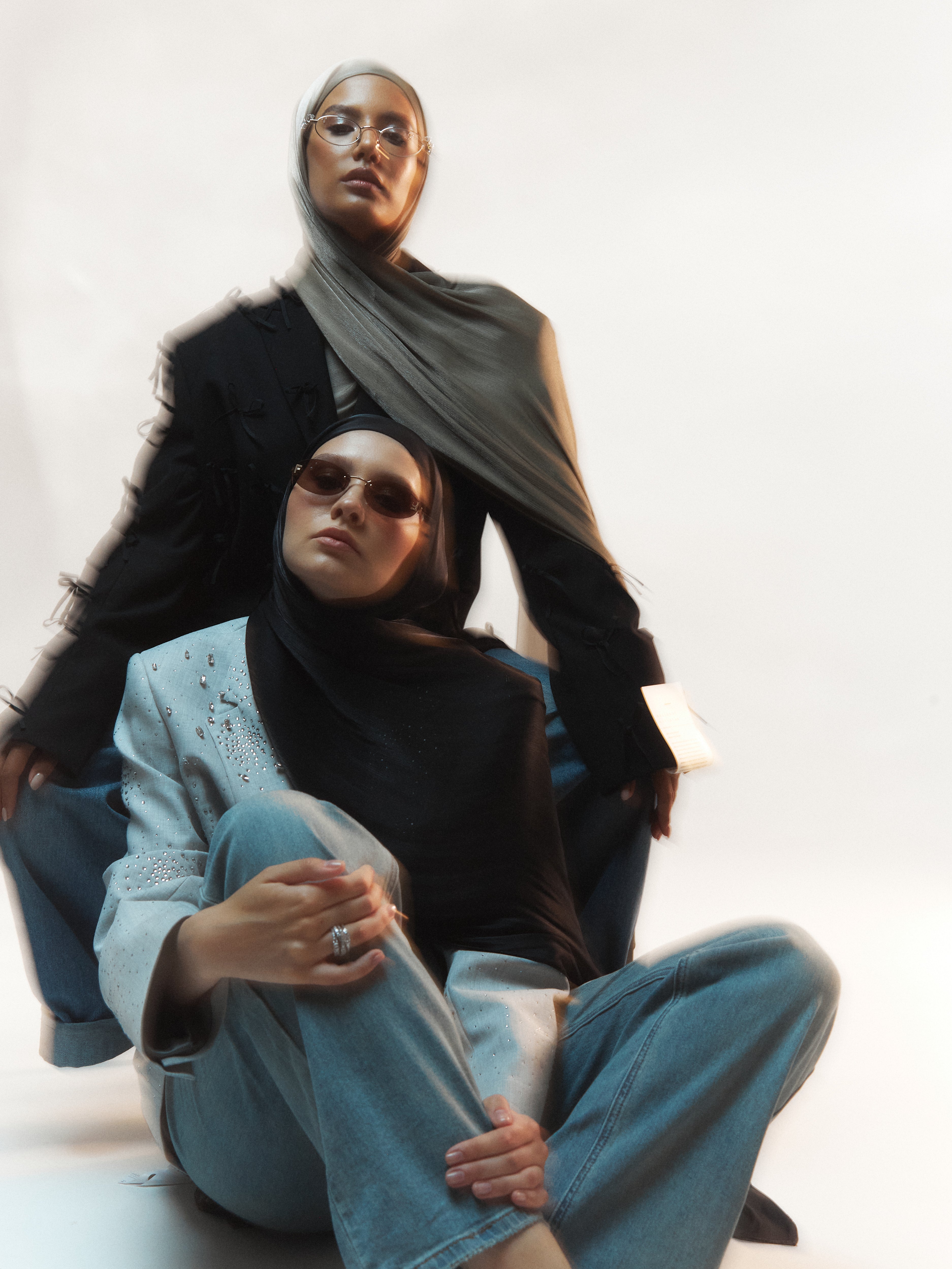 Two women wearing black silk hijabs from Yovlaq, styled in contrasting embellished blazers and denim – bold and modern modest fashion editorial.