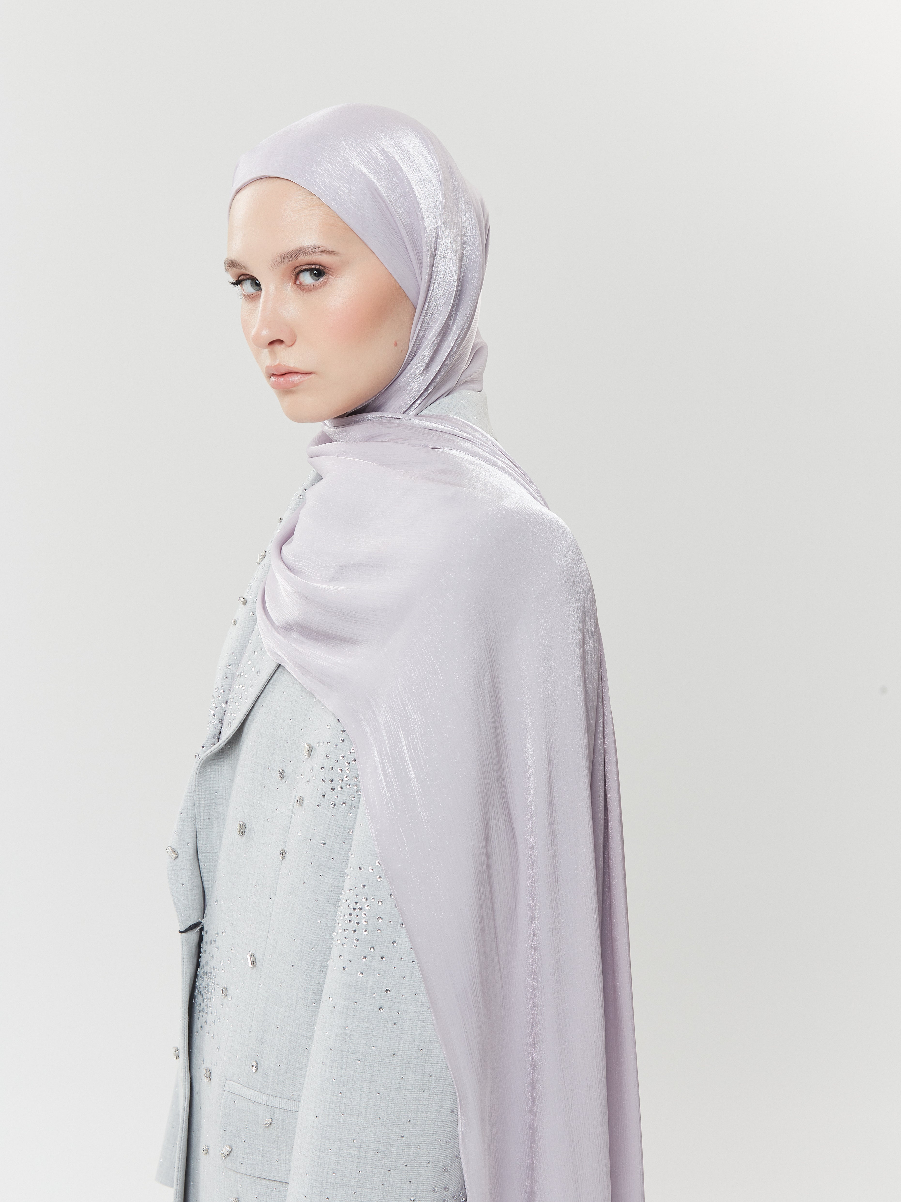 Elegant woman in pale lavender silk hijab by Yovlaq, styled with a beaded soft grey abaya – graceful modest fashion for special occasions.