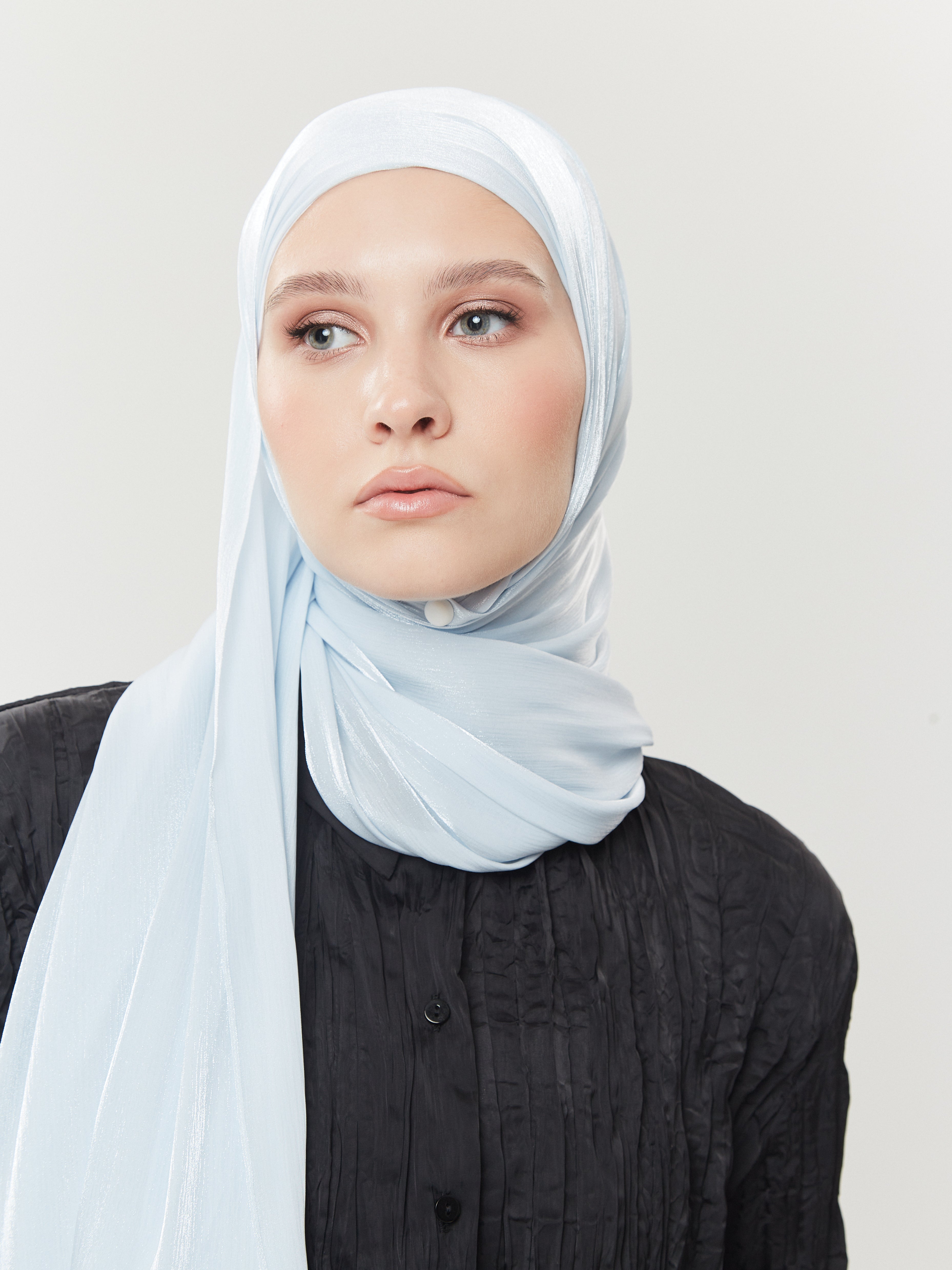 Woman wearing pastel blue silk hijab by Yovlaq styled over a black textured blouse – soft shimmer and graceful drape for modern modest fashion.