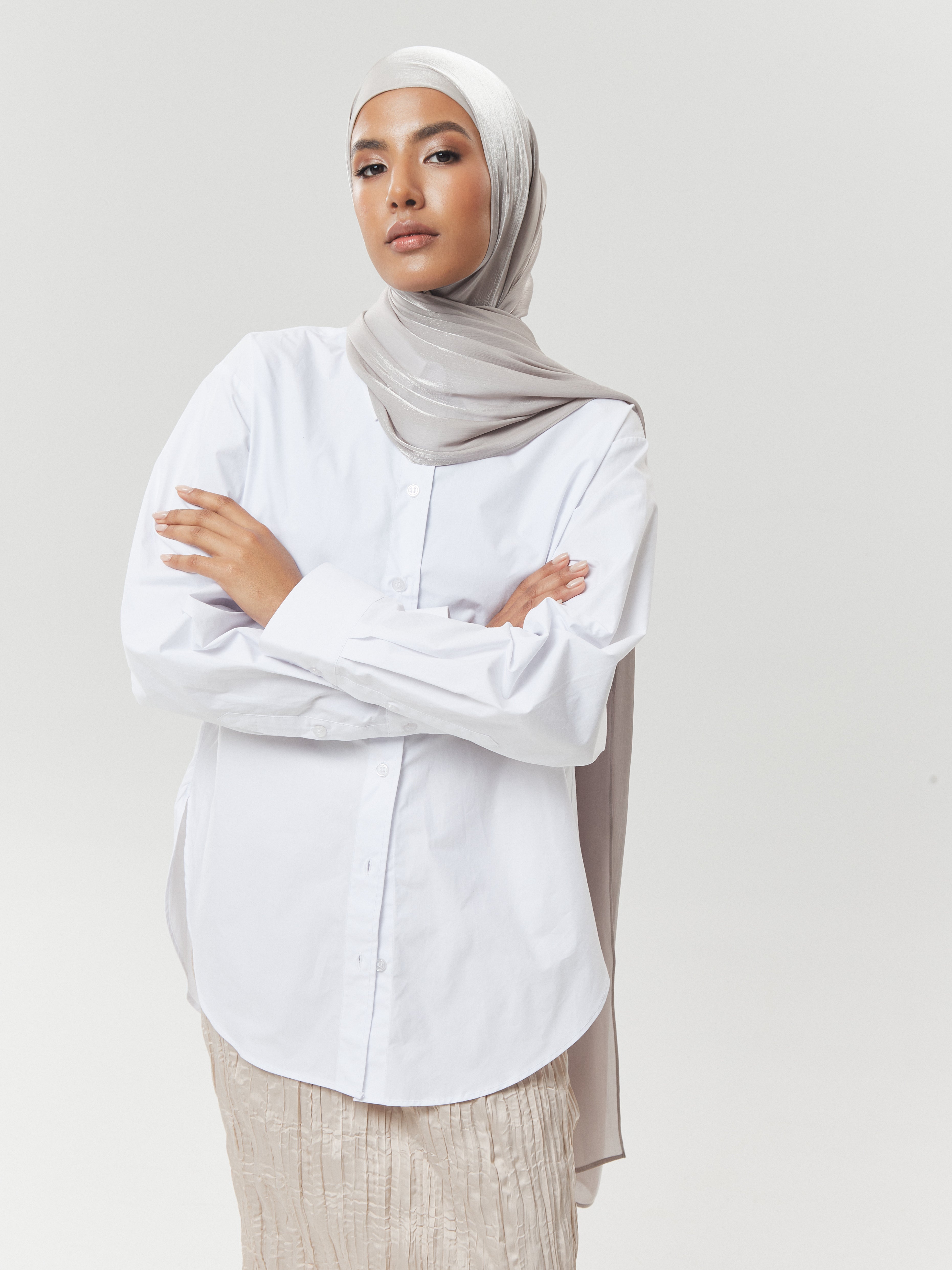Woman wearing taupe grey silk hijab from Yovlaq styled with a white oversized shirt and crinkled beige skirt – minimalist modest fashion look.