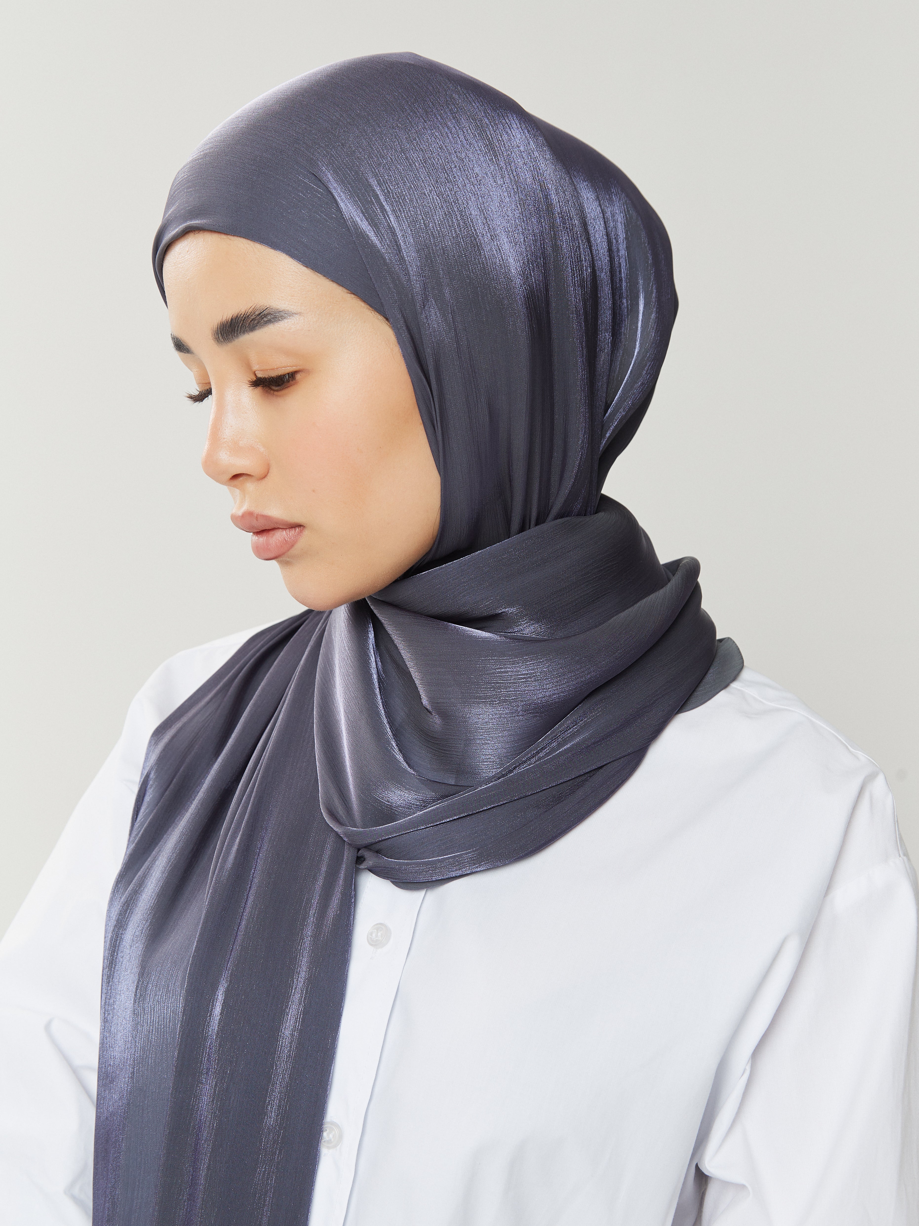 Side profile of woman wearing Yovlaq midnight blue silk hijab with subtle shimmer, paired with a crisp white shirt – elegant and contemporary modest fashion.