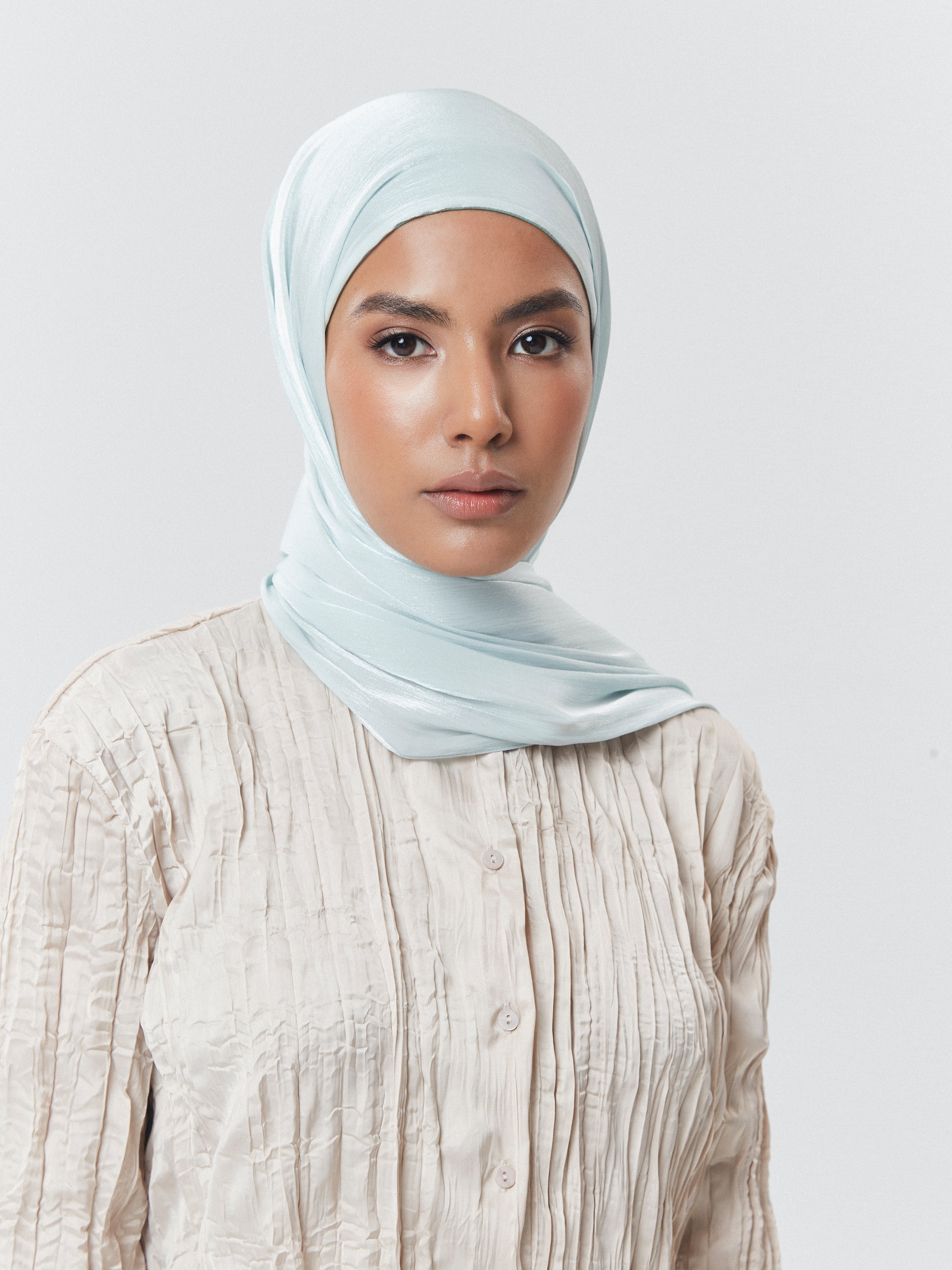 Woman wearing Yovlaq light blue chiffon hijab styled neatly over a cream textured blouse – breathable and elegant modest fashion accessory.