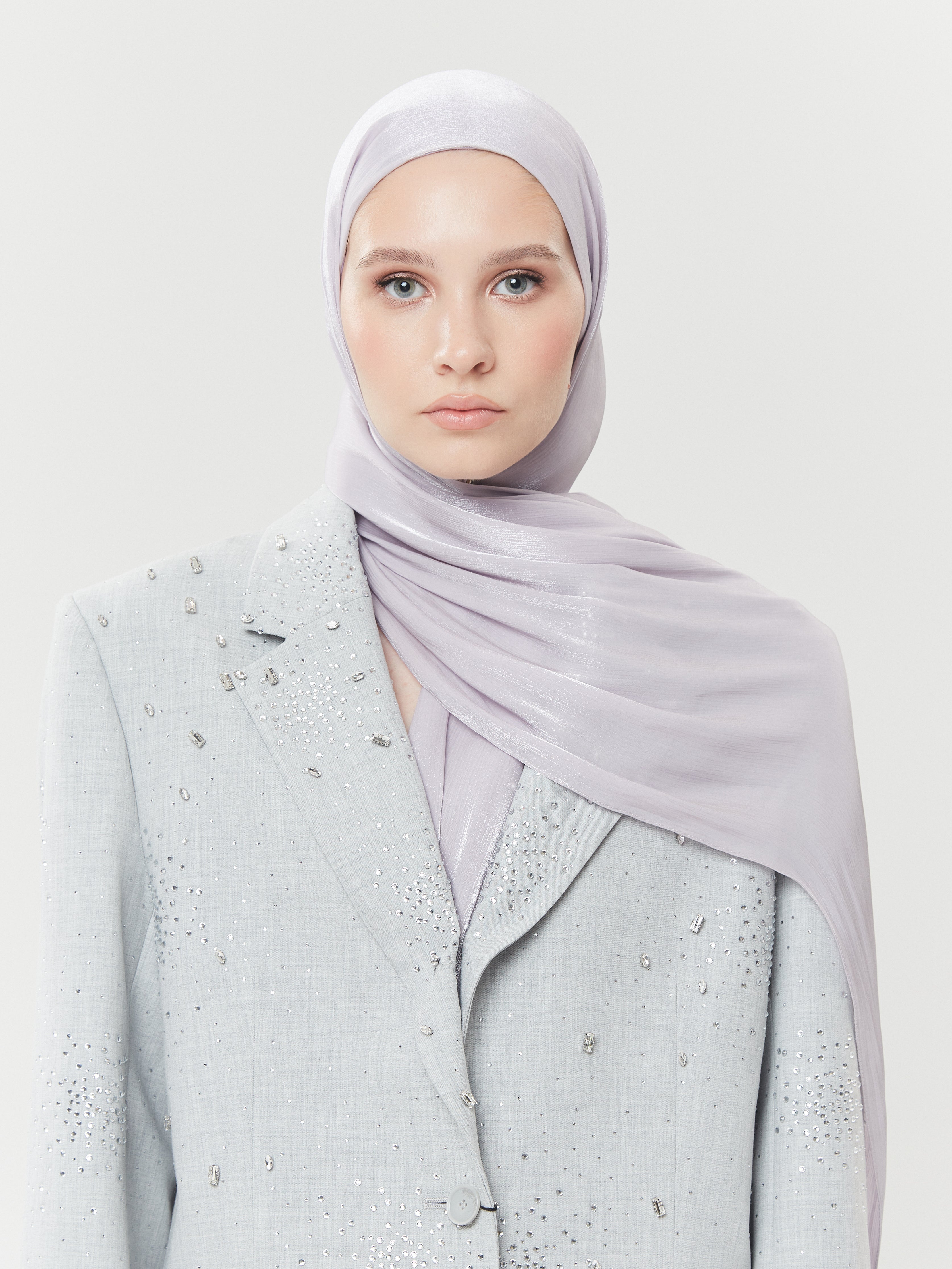 Front view of woman wearing pale lavender silk hijab by Yovlaq, paired with a light grey embellished blazer – elegant and polished modest fashion.