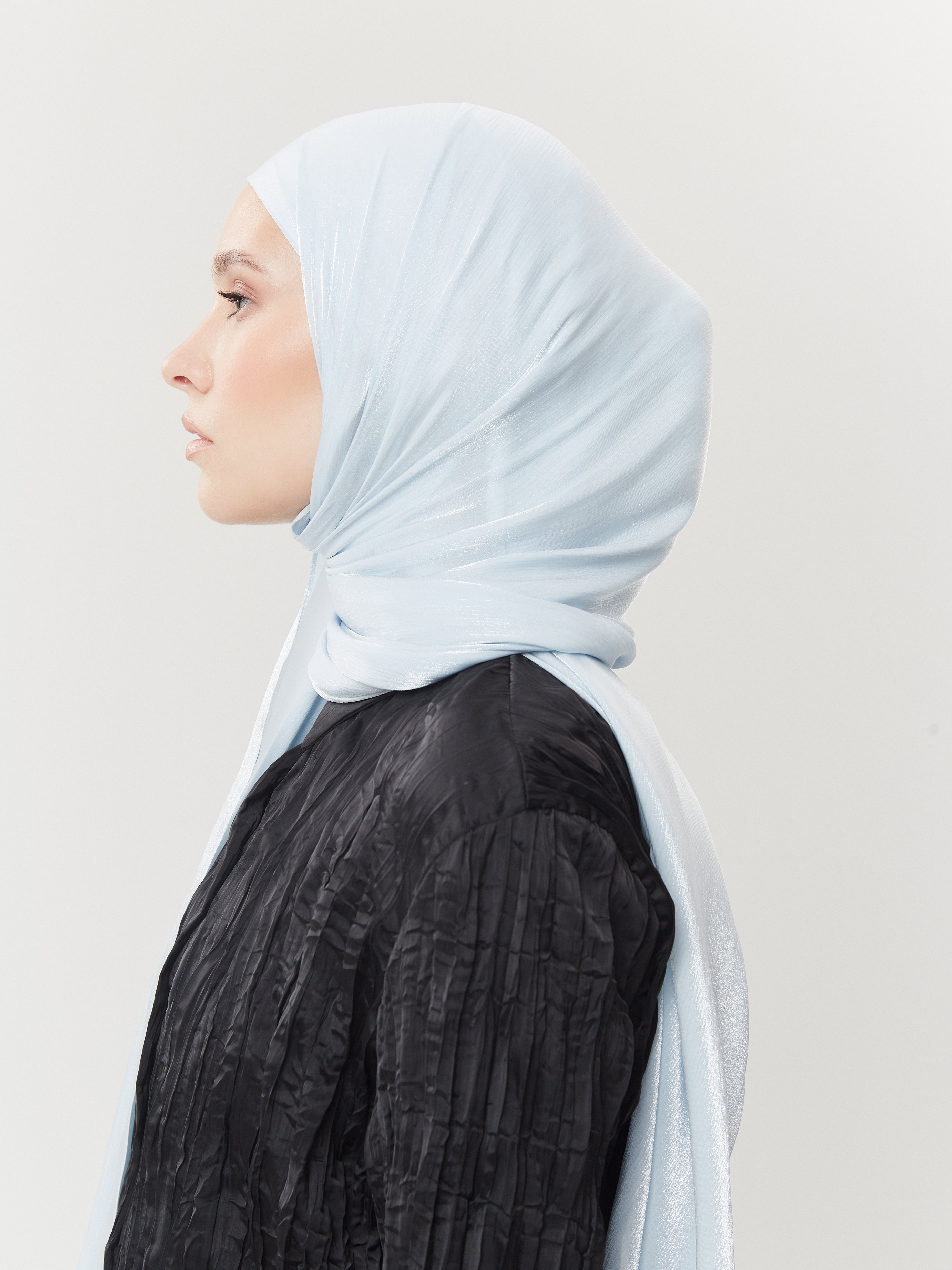 Side profile of woman wearing pastel blue silk hijab from Yovlaq tied at the back – styled with a pleated black blouse for a contemporary modest look.