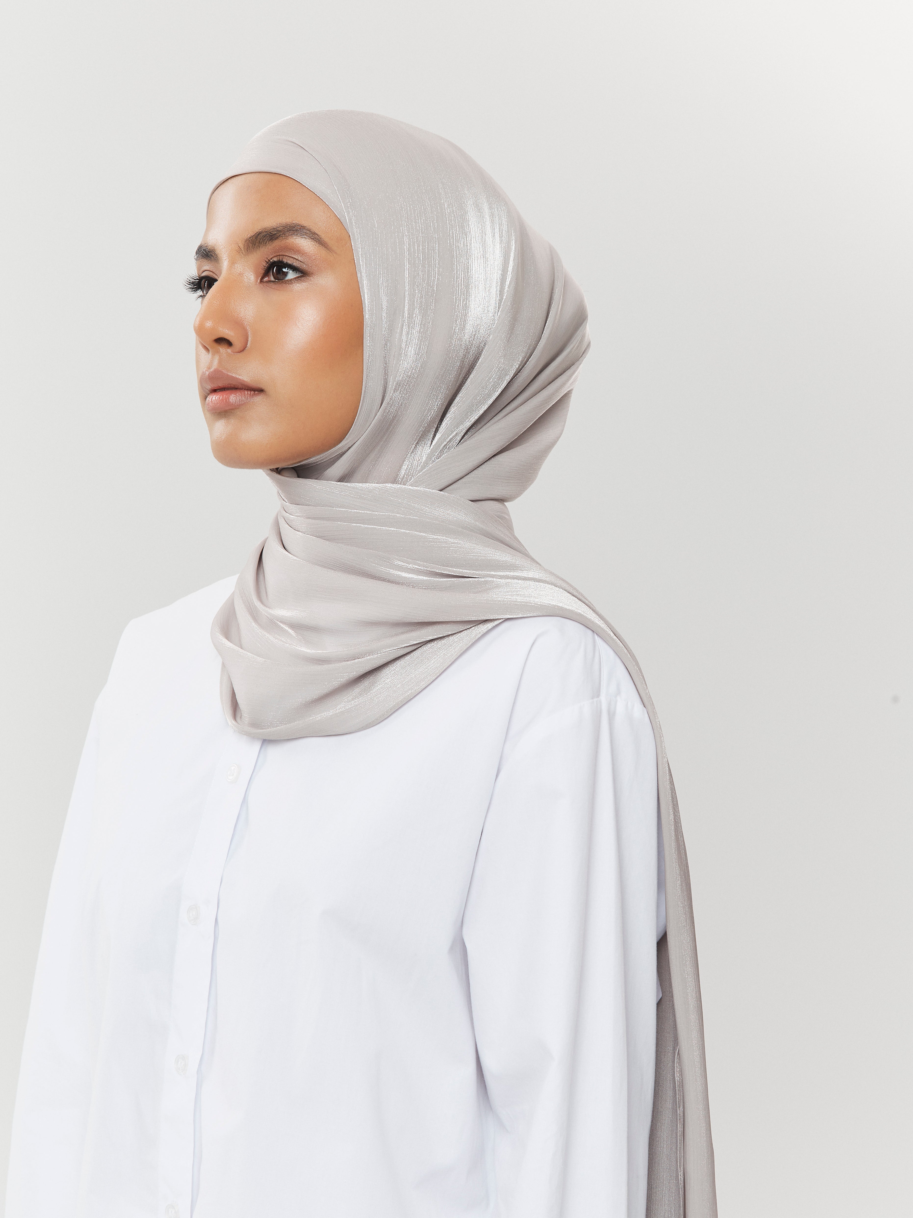 Side view of woman wearing silver-grey silk hijab from Yovlaq styled with a crisp white shirt – sleek and minimal modest fashion look.
