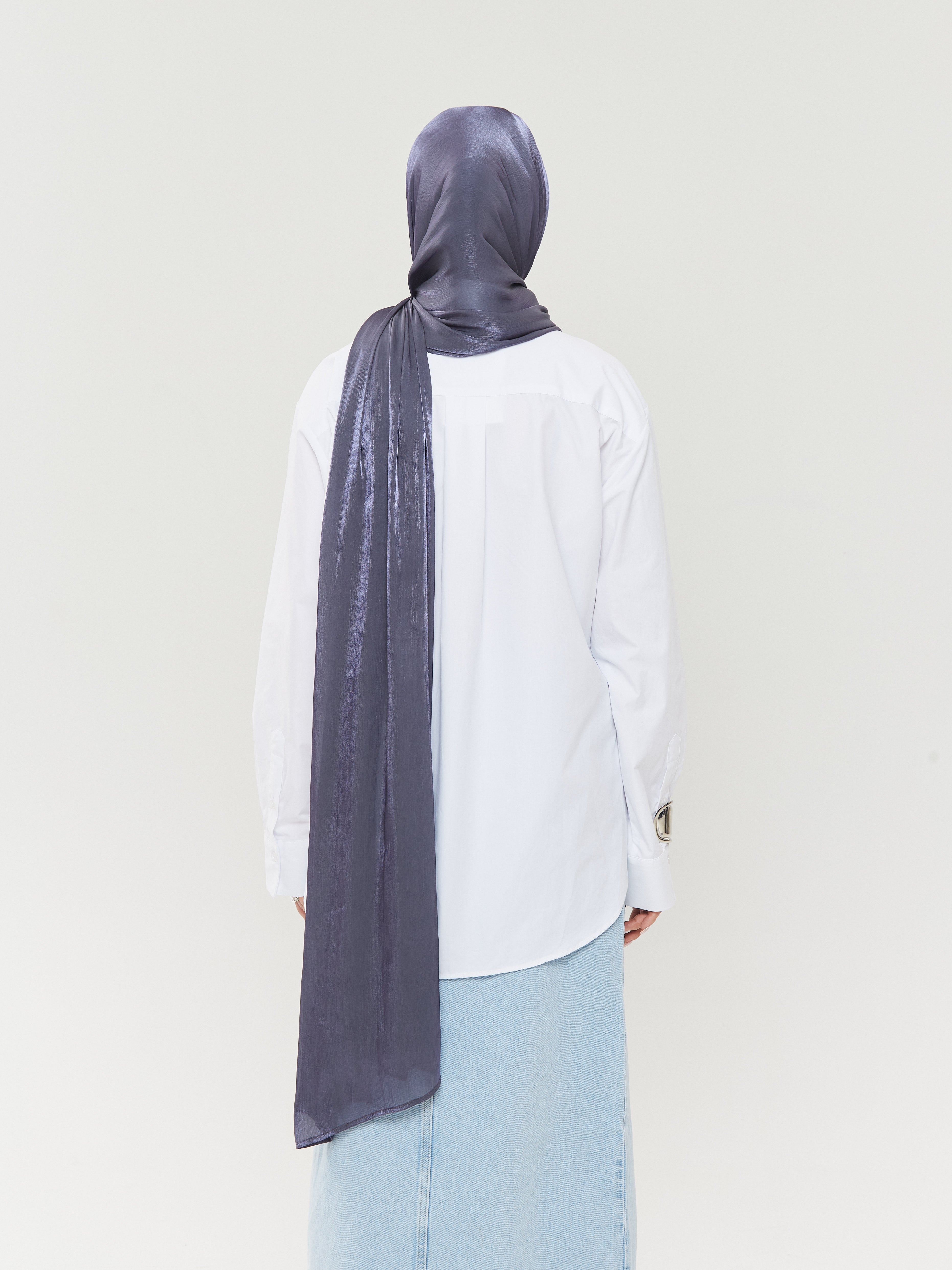 Back view of woman wearing Yovlaq midnight blue silk hijab styled with a long drape – paired with white shirt and blue textured skirt for a modest modern look.