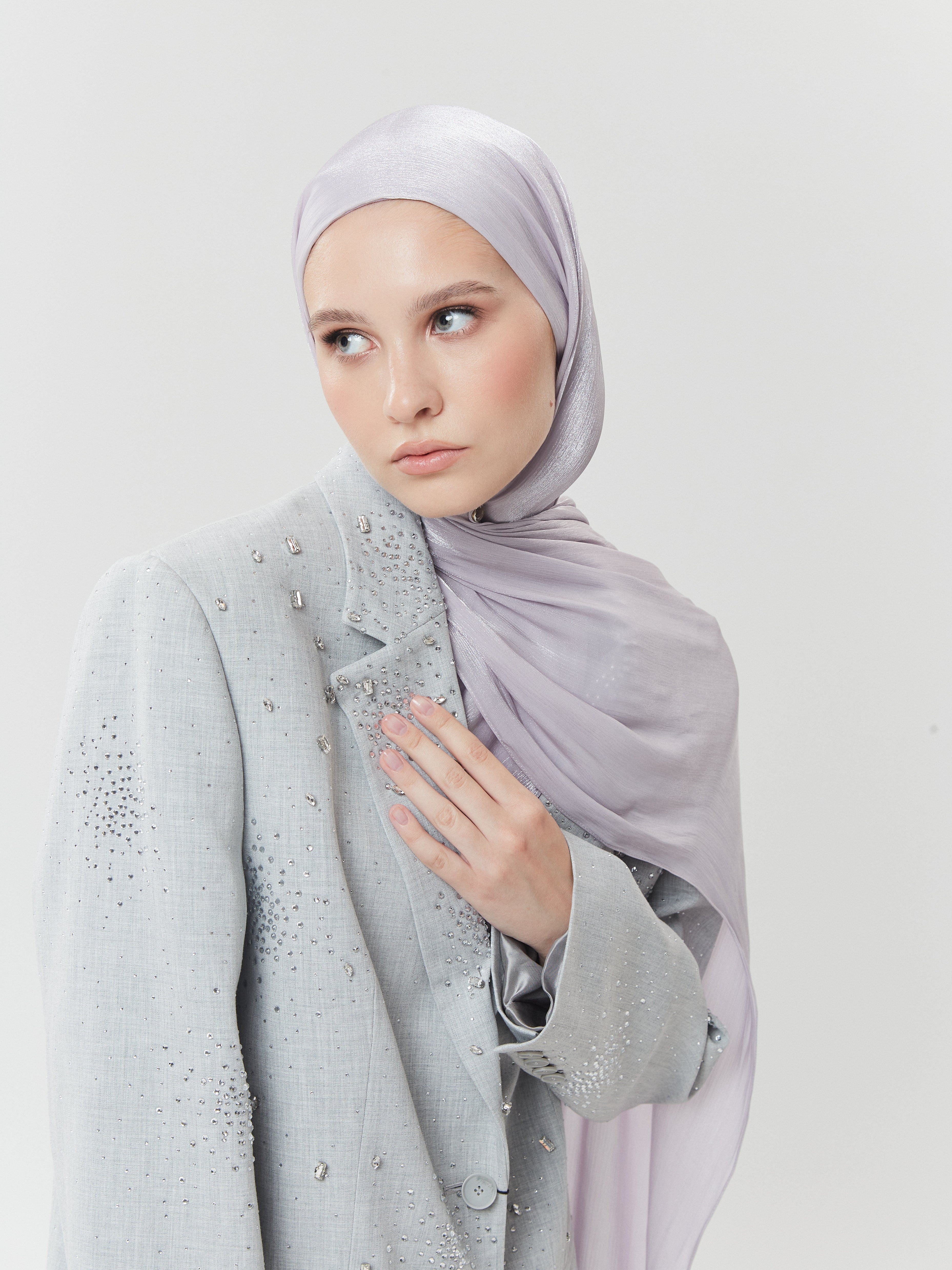 Woman wearing pale lavender silk hijab from Yovlaq with hand over embellished light grey blazer – graceful modest fashion for formal occasions.
