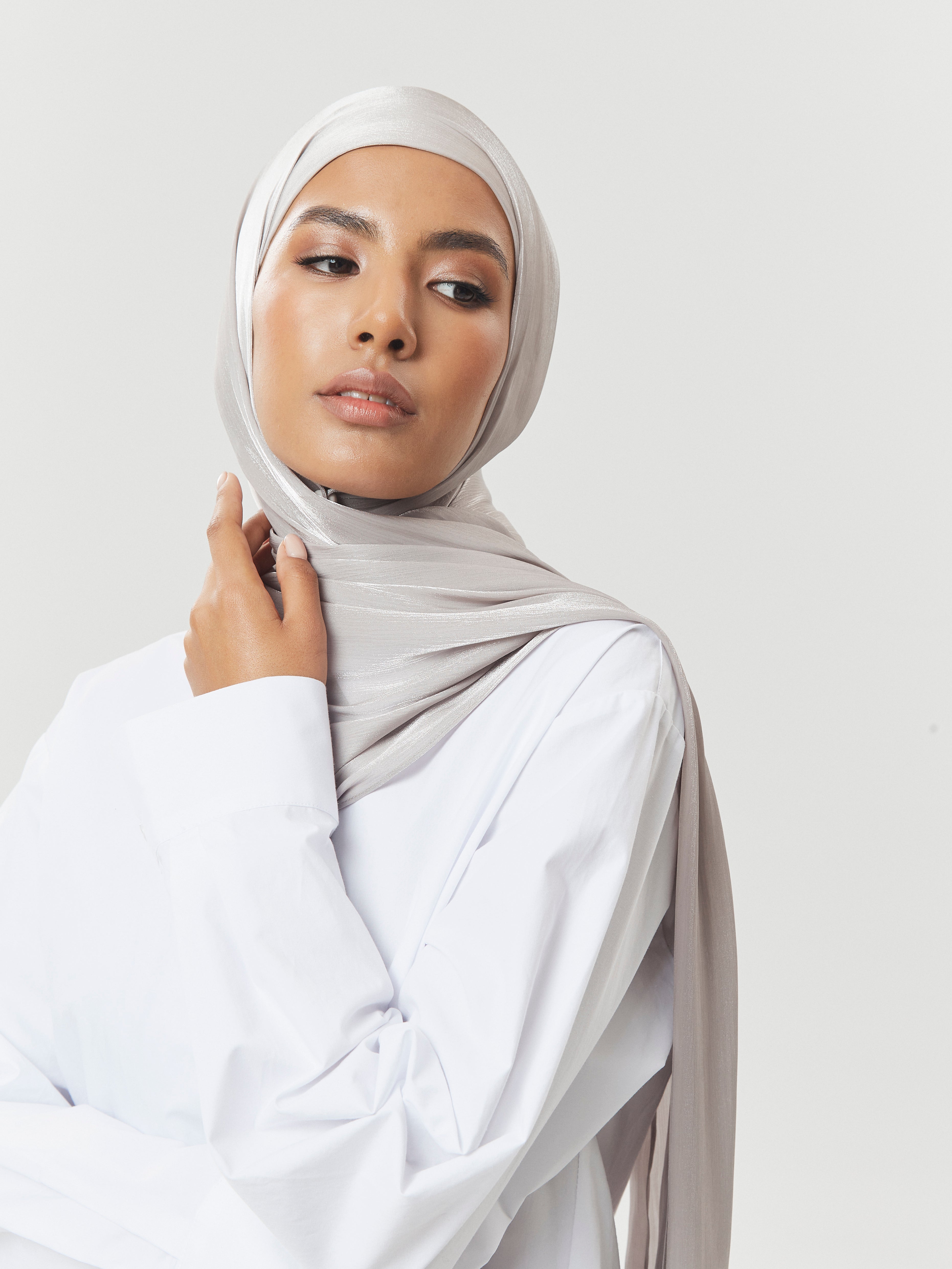 Confident woman wearing silver-grey silk hijab by Yovlaq paired with white shirt – subtle shimmer and modern modest fashion styling.