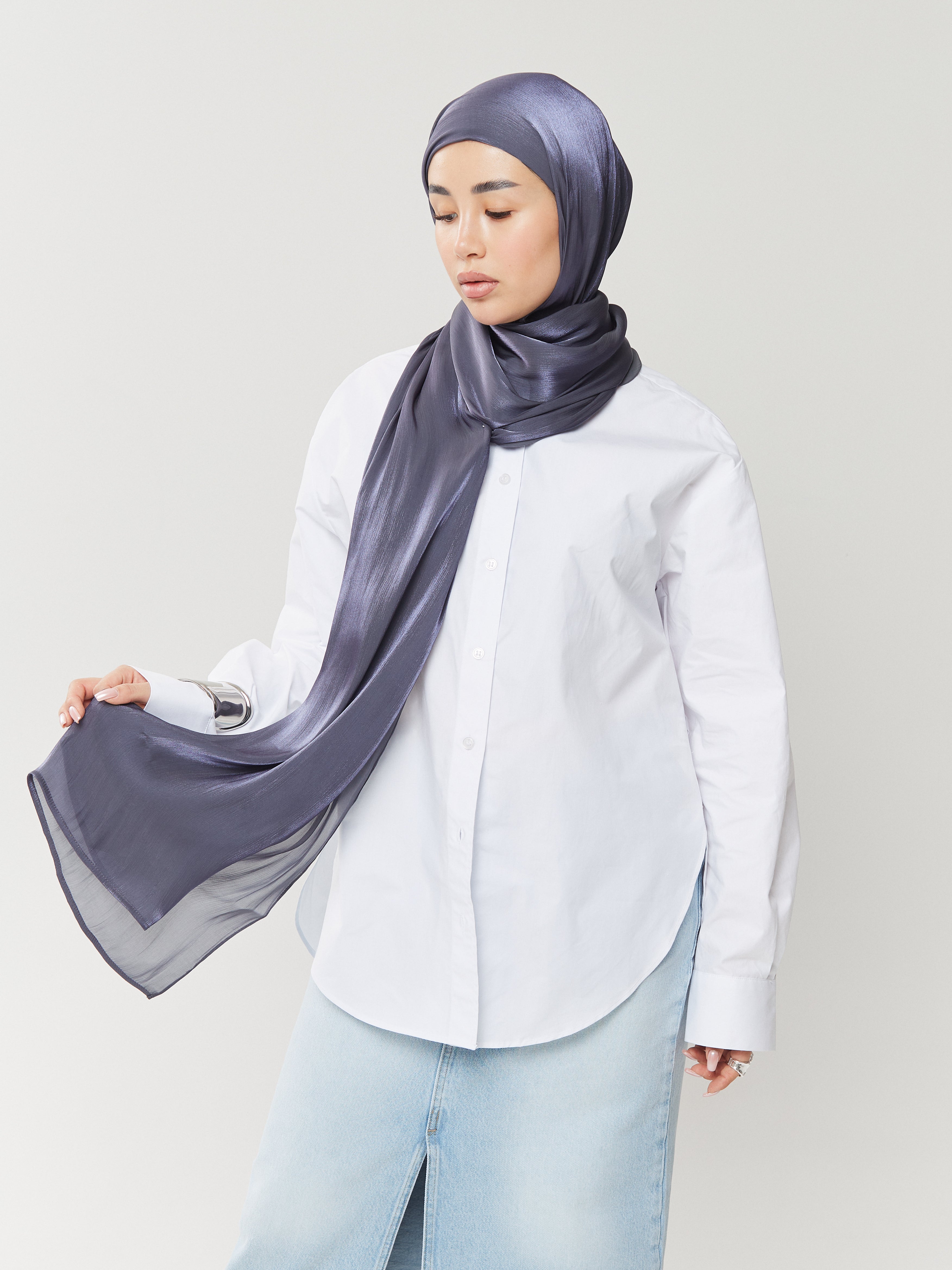 Woman wearing Yovlaq midnight blue silk hijab styled with a white shirt and light denim skirt – fluid drape and soft shimmer in motion.