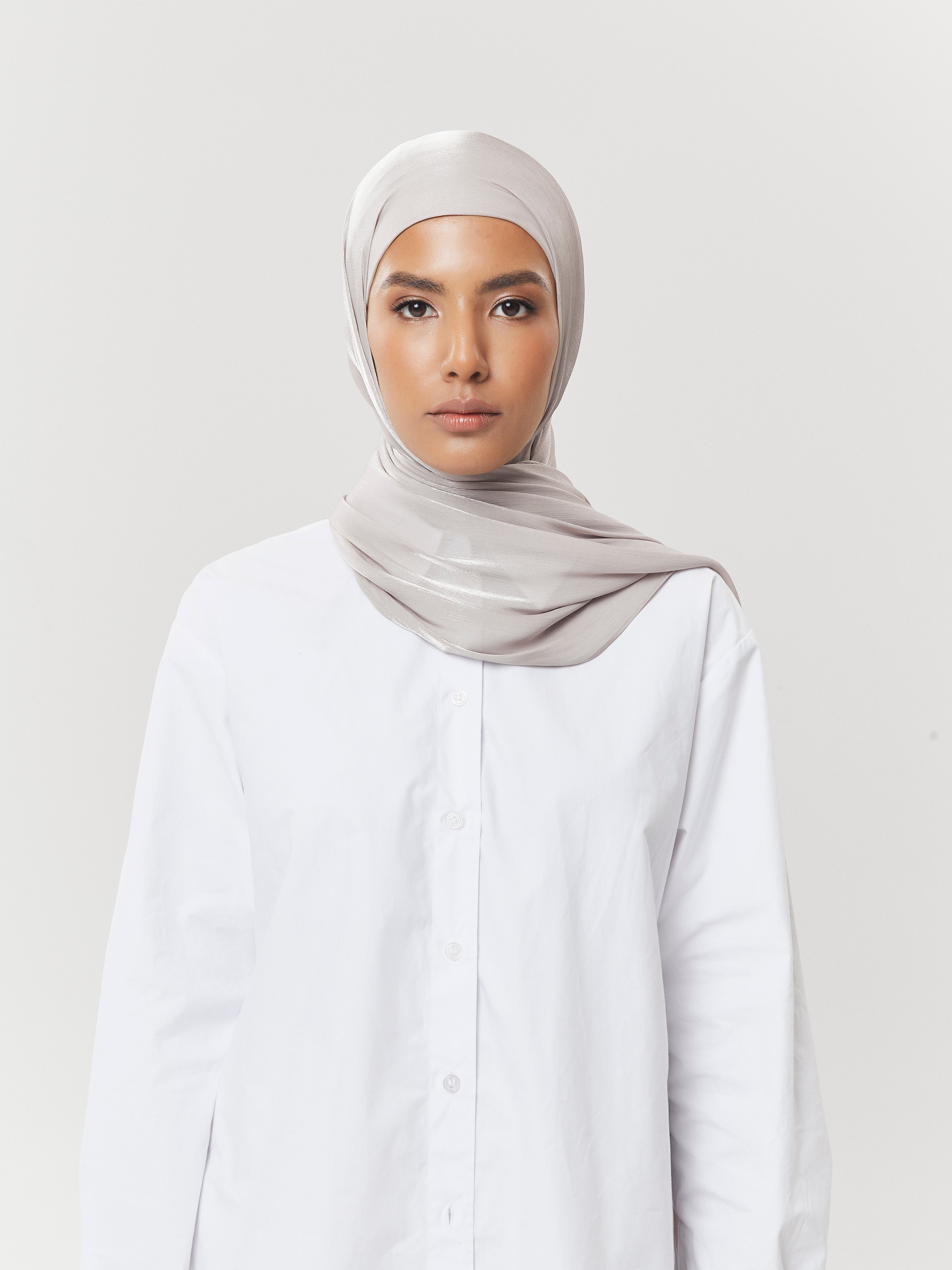 Front view of woman wearing silver-grey silk hijab from Yovlaq styled with a white button-down shirt – sleek and refined everyday modest fashion.