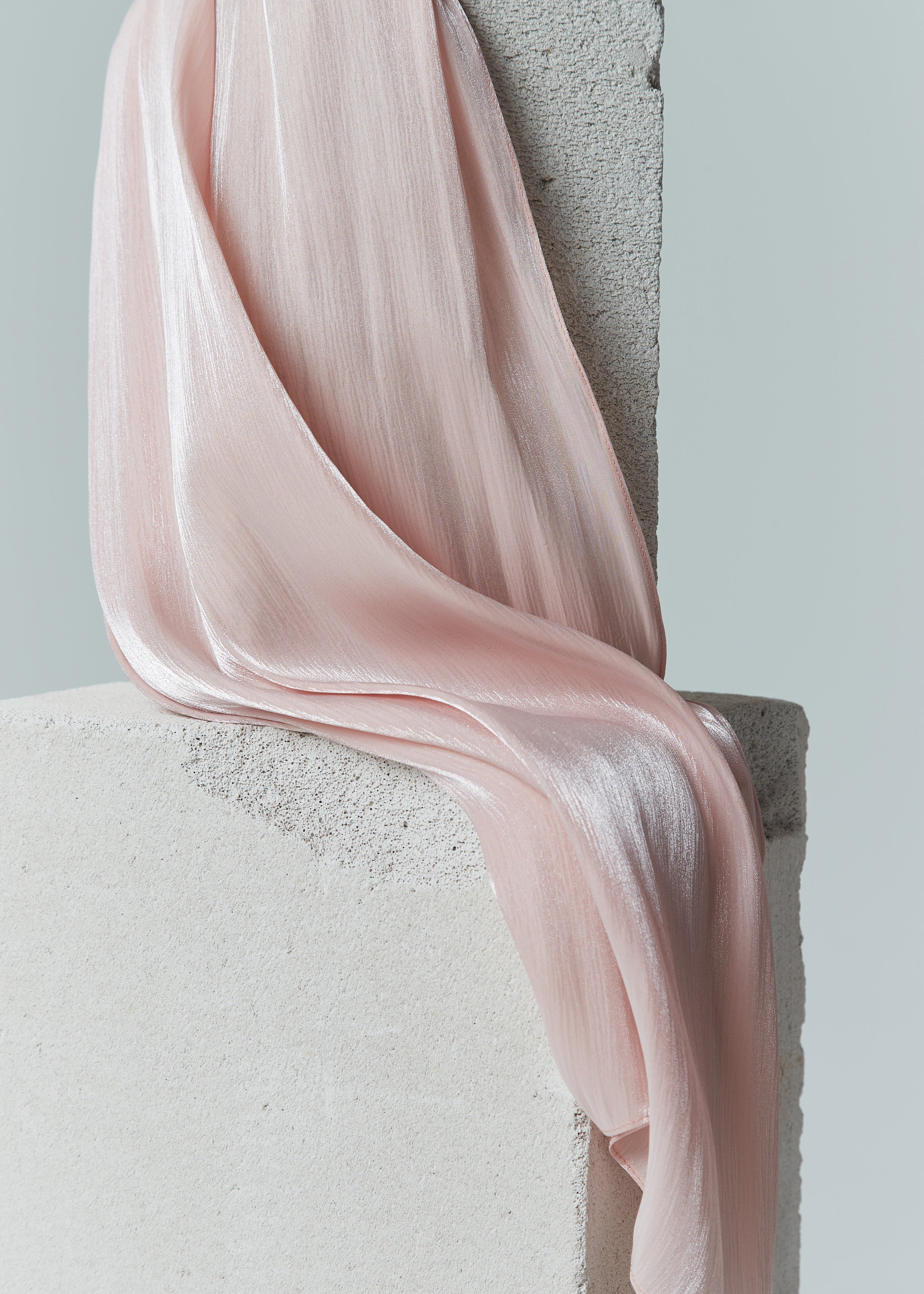 Close-up of pastel pink rose silk hijab from Yovlaq draped over concrete blocks – soft, lightweight fabric with a luminous sheen.