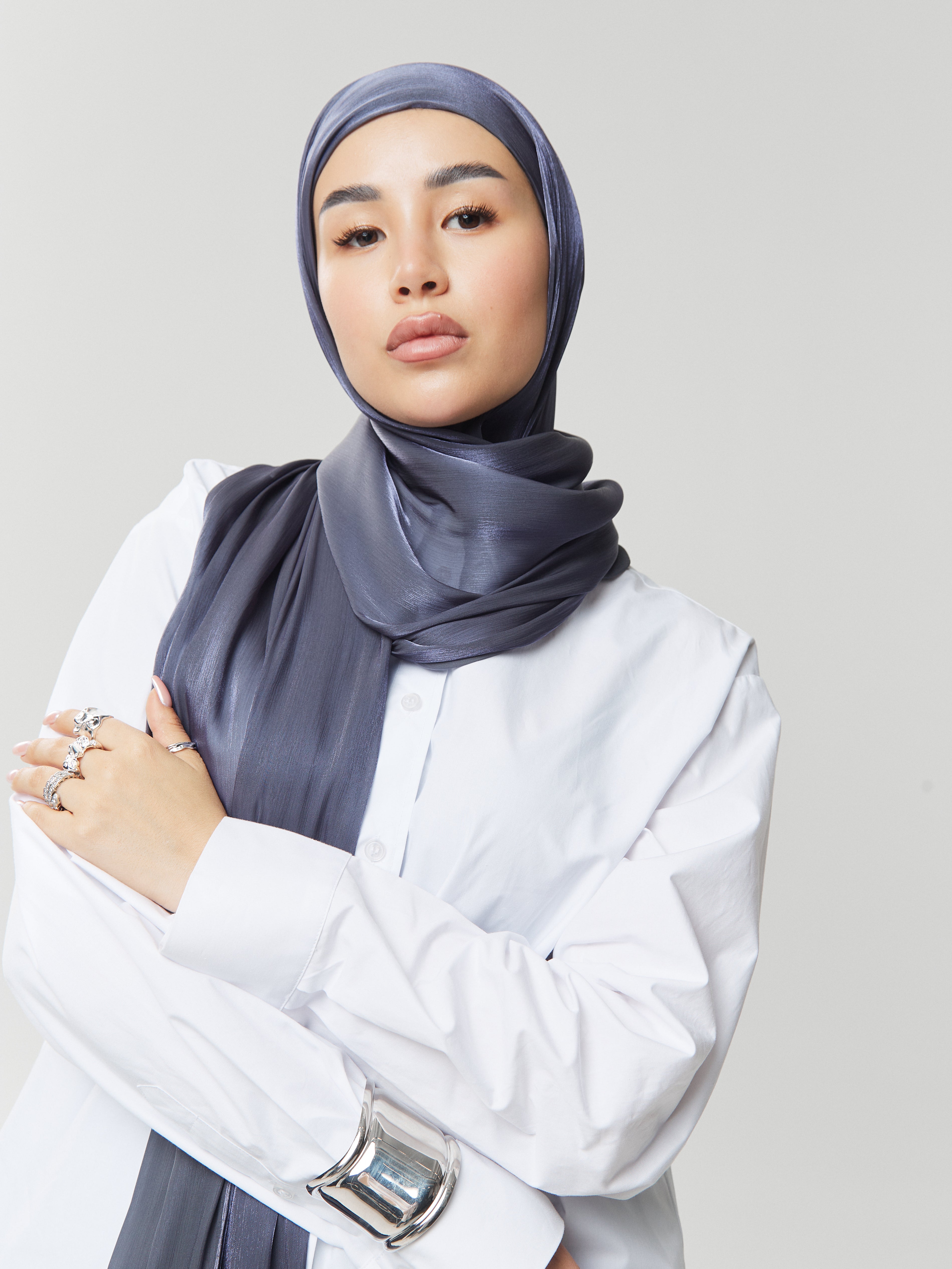 Confident woman wearing Yovlaq midnight blue silk hijab styled with a crisp white shirt and silver jewelry – modern and elegant modest fashion.