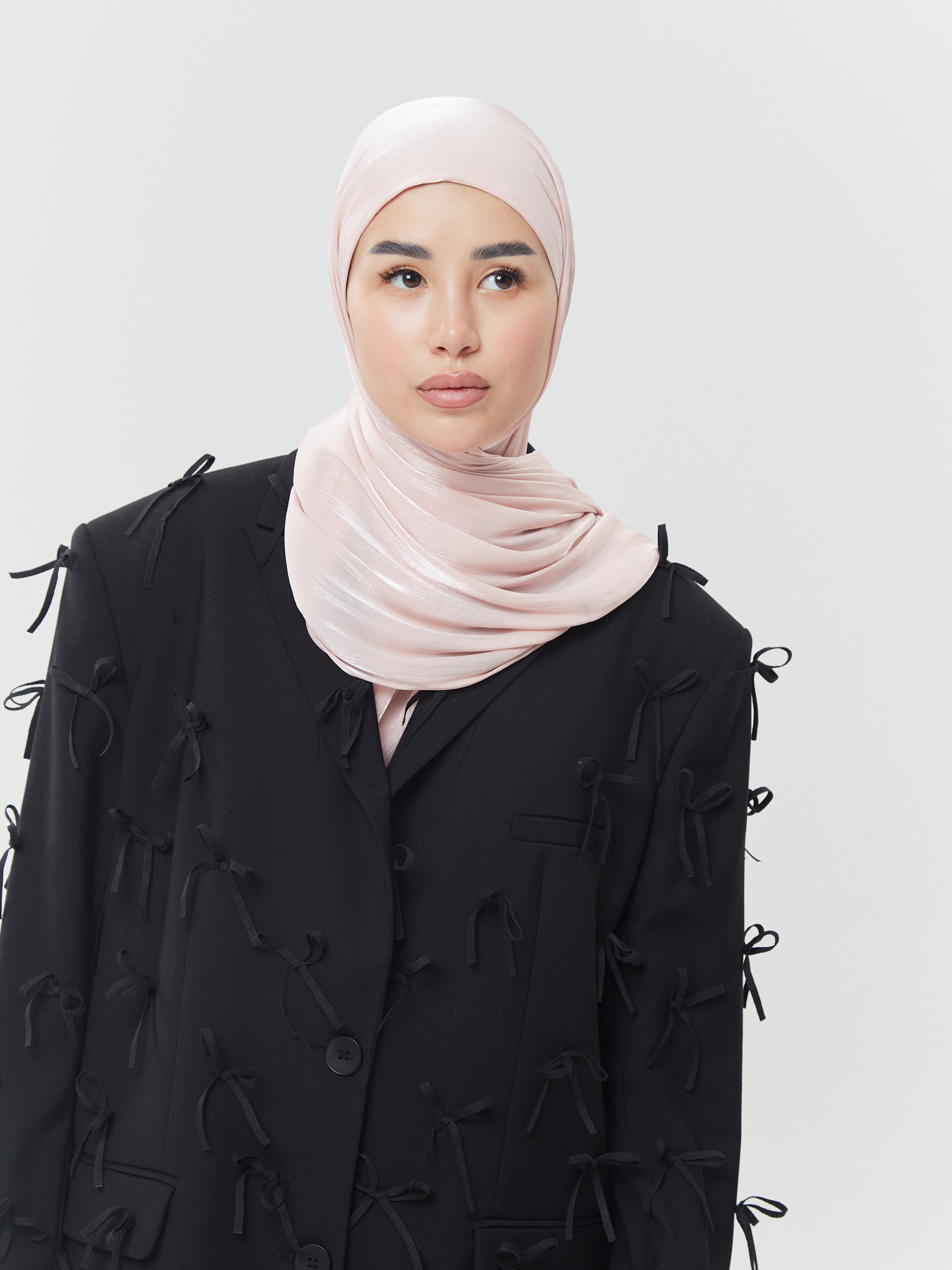 Woman wearing pastel pink rose silk hijab from Yovlaq styled with a black blazer adorned with bows – elegant contrast in modern modest fashion
